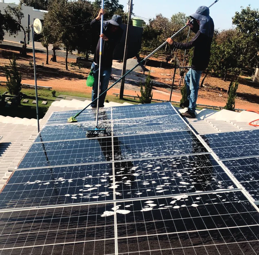 Dois técnicos da Aliança lavando módulos fotovoltaicos com rodo e cabo extensor sobre um telhado.