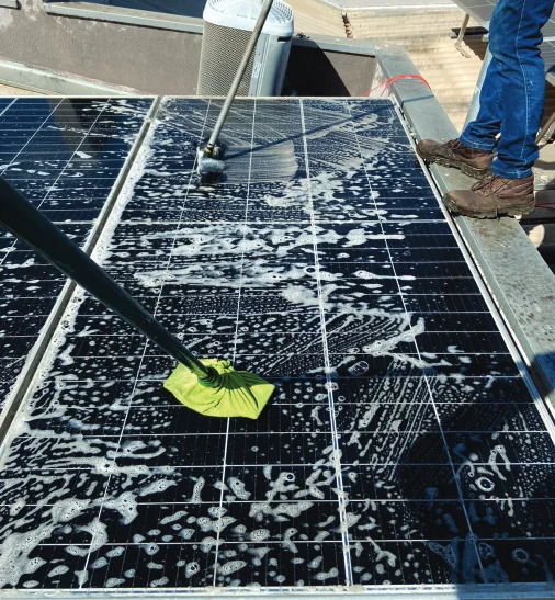 Detalhe de módulo fotovoltaico sendo lavado com espuma e rodo.